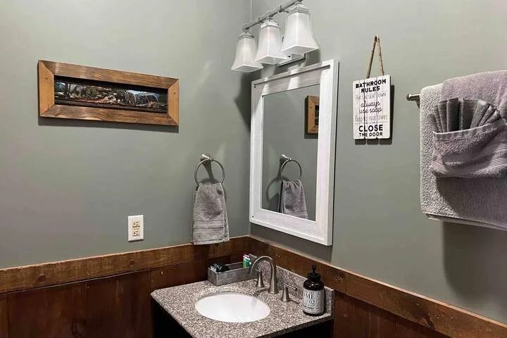 Bathroom vanity with a granite top, a white-framed mirror and wood wainscoting
