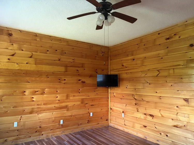 Pine-paneled corner room with a ceiling fan and a small wall TV