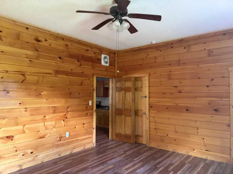 Pine-paneled room with a ceiling fan, looking through to the kitchen